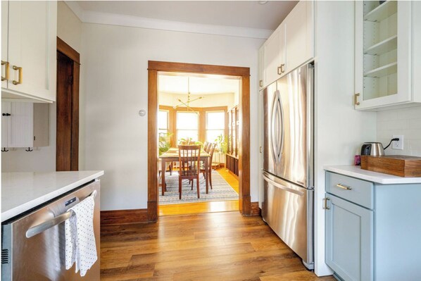 Una cocina con piso de madera, gabinetes blancos, un refrigerador de acero inoxidable y un comedor con mesa y sillas.