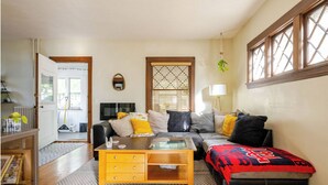 A living room with a sofa, coffee table, and ottoman. There is a window with blinds, a lamp, and a plant.