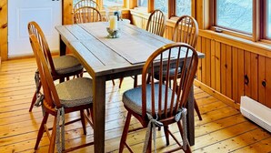 A wooden dining room with a large table and chairs, large windows, and hanging pendant lights.