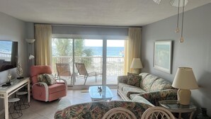 A living room with a sofa, armchair, and coffee table, a TV, and a balcony with a view of the beach. - Driftwood Towers 2 bedroom unit 2C. Gulf front condo in Gulf Shores Alabama. (Gulf Shores)
