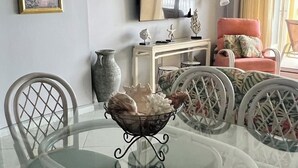 A dining area with a glass table surrounded by wicker chairs, a vase with decorative items, and a television on the wall. - Driftwood Towers 2 bedroom unit 2C. Gulf front condo in Gulf Shores Alabama. (Gulf Shores)