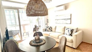 A modern living room with a round dining table, two chairs, a sofa, and a large woven rug. - Casa Caramona - Two Bedroom Apartment, Sleeps 4 (Nerja)