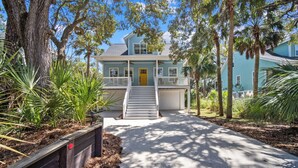 A two-story house with a front porch, a garage, and a driveway leading to the entrance. - Quiet Retreat, Golf Cart Included, Pet Friendly - 603 Porpoise (Fripp Island)
