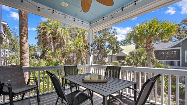 A covered outdoor seating area with a table and chairs, surrounded by a white railing, overlooking a residential neighborhood with palm trees and houses. - Quiet Retreat, Golf Cart Included, Pet Friendly - 603 Porpoise (Fripp Island)
