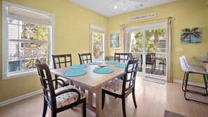 A dining area with a table set for six, surrounded by chairs with patterned cushions, a ceiling fan, and a view of the outdoors through large windows. - Quiet Retreat, Golf Cart Included, Pet Friendly - 603 Porpoise (Fripp Island)