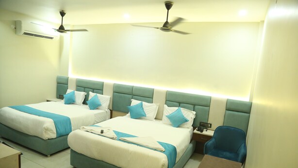 A hotel room with two beds, a desk, and a chair. There are ceiling fans and an air conditioning unit. - Hotel Greenland (Khammam)