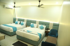 A hotel room with two beds, a desk, and a chair. There are ceiling fans and an air conditioning unit. - Hotel Greenland (Khammam)