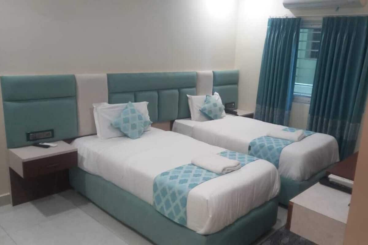 A hotel room with two beds, a nightstand, a desk, and a window with curtains.