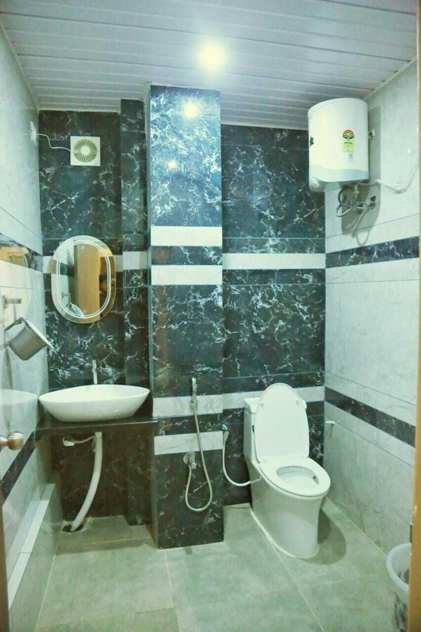 A bathroom with a sink, mirror, toilet, and a water heater. - Hotel Greenland (Khammam)