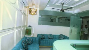 A modern living room with a sectional sofa, a fish tank, and a ceiling fan. - Hotel Greenland (Khammam)