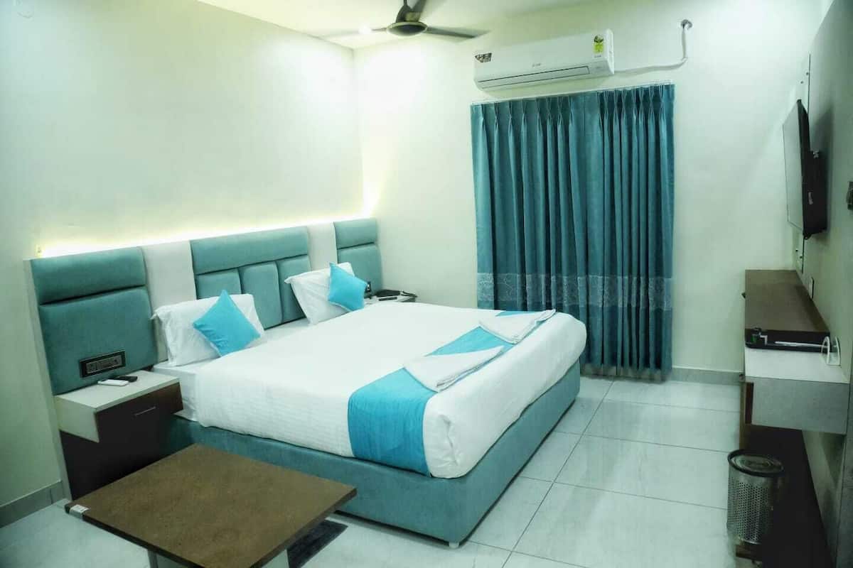 A hotel room with a bed, bedside tables, a desk, an air conditioning unit, a television, and a curtain.