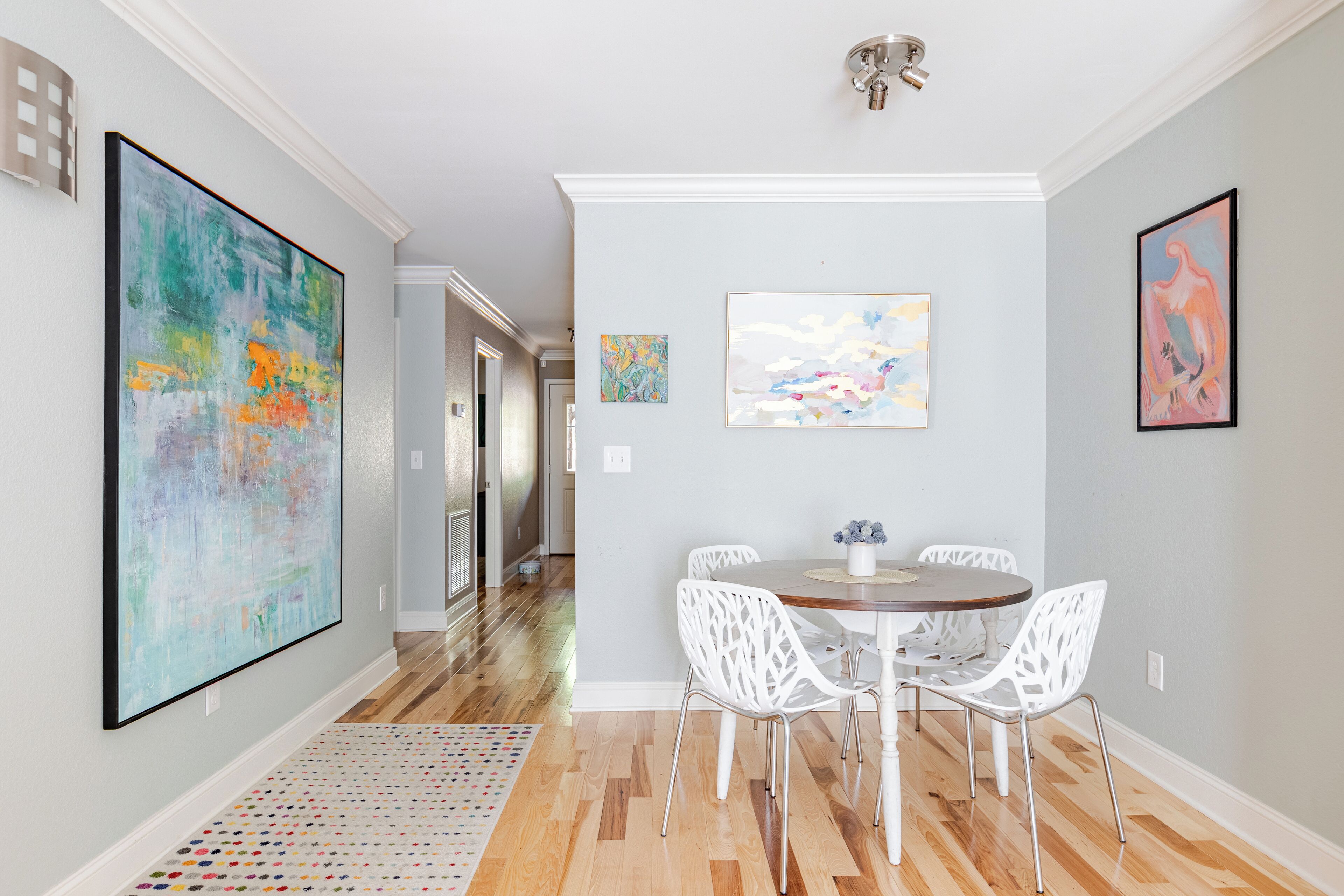 A dining area with a round table, white chairs, and artwork on the walls.