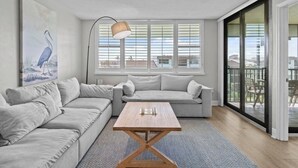 A modern living room with a grey sofa set, a wooden coffee table, and a large window with blinds. - Perfect Beach Vacation -Sanibel Island's Loggerhead Cay 234 (Sanibel)