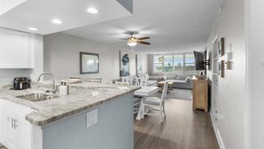 A modern kitchen with a central island, white cabinetry, and a dining area with a gray sofa. - Perfect Beach Vacation -Sanibel Island's Loggerhead Cay 234 (Sanibel)
