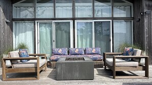 Un edificio moderno de madera con amplios ventanales y una terraza con un conjunto de sofás y dos sillones.