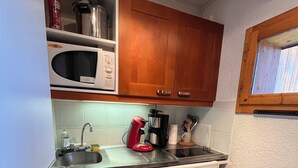 A compact kitchen with wooden cabinets, a microwave, a coffee maker, and a dishwasher.
