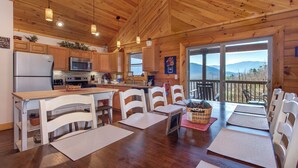 Une cuisine rustique aménagée dans une cabane en bois, équipée d’un réfrigérateur, d’un four à micro-ondes et d’une cuisinière. On y trouve des chaises blanches et une table à manger.