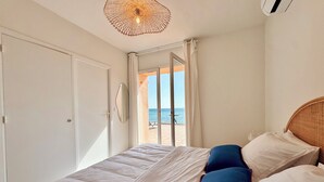 Un dormitorio con cama, una lámpara en el techo, vista al mar a través de una ventana y una puerta.