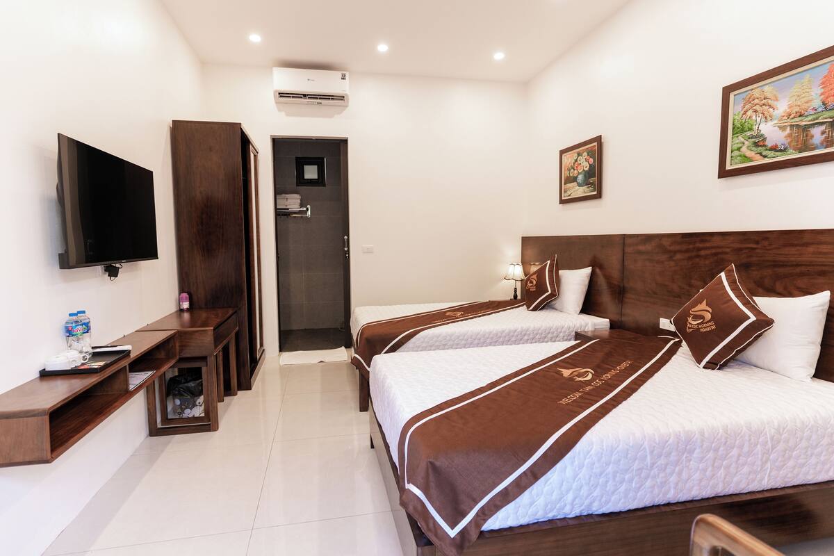 A hotel room with two beds, a TV, a desk, and a door leading to a bathroom.