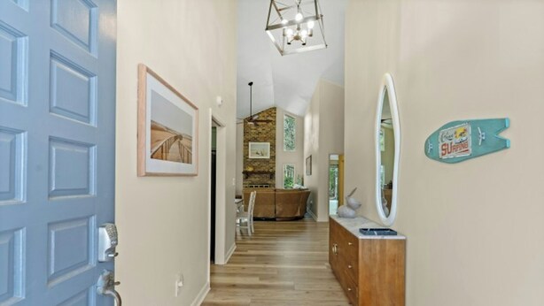 Un couloir avec une porte bleue, une commode en bois, un miroir et une décoration représentant une planche de surf.