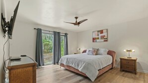 Une chambre à coucher comprenant un lit, des tables de chevet, un ventilateur de plafond et une vue sur l’extérieur par une fenêtre.