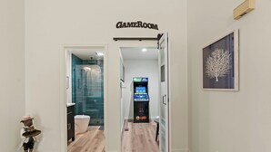 Un couloir menant à une salle de bain équipée d’une douche, de toilettes et d’une console de jeux.