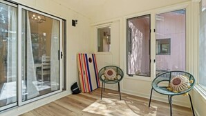 Une pièce avec un plancher en bois, deux chaises dotées de coussins à motifs, un tableau rayé et une porte-fenêtre coulissante.