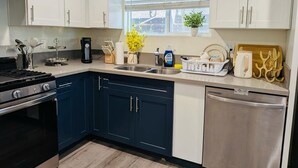 Une cuisine moderne avec des meubles blancs, un mur d’accent bleu, des appareils en acier inoxydable et une fenêtre avec des stores.