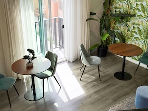 Una sala de estar moderna con una mesa redonda de madera, dos sillas, un bonsái en maceta y una planta grande.
