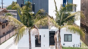 Un bâtiment moderne à deux étages, doté d’un toit plat, de grandes fenêtres et d’un petit jardin à l’avant, agrémenté de palmiers.