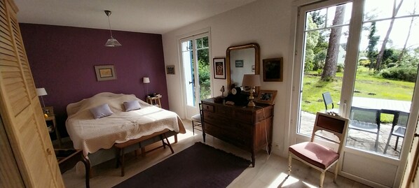 A bedroom with a bed, dresser, chair, and a large window with a view of greenery.