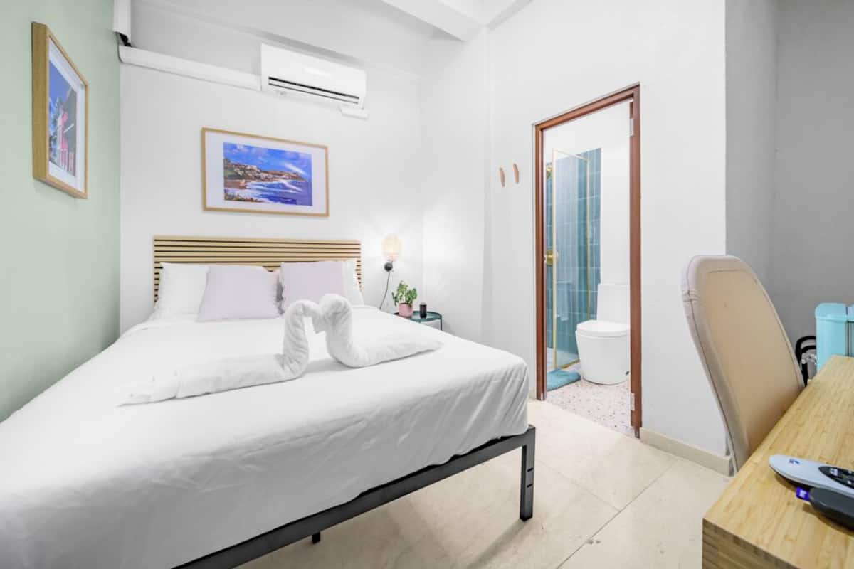 A hotel room with a bed, a desk, an air conditioner, and a bathroom visible through an open door.