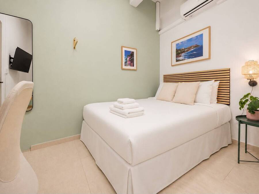 A hotel room with a bed, a chair, a bedside table with a lamp, and a wall-mounted TV.