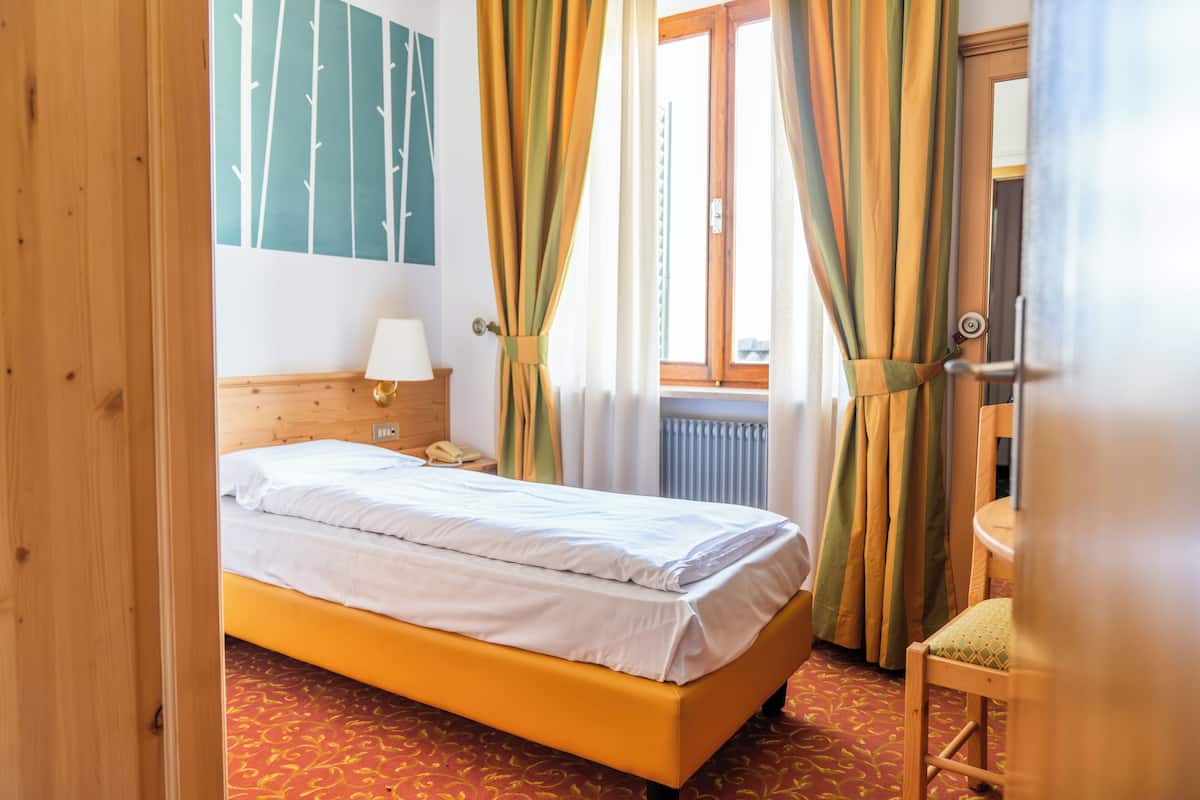 A bedroom with a bed, a nightstand, a lamp, a chair, and a window with curtains.