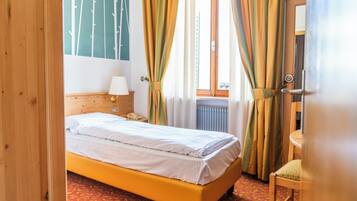 Un dormitorio con cama, mesita de noche, lámpara, una silla y ventana con cortinas.