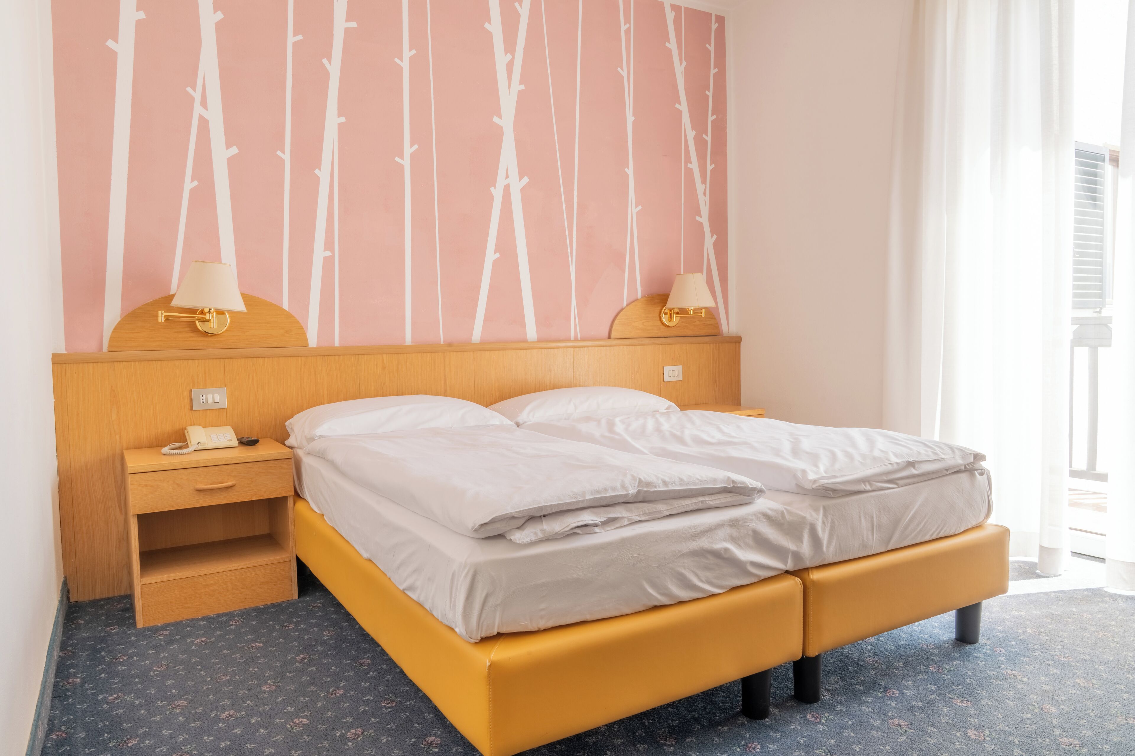 Una cama bien tendida con un cabecero de madera, una mesita de noche con una lámpara y una pared con un diseño de bambú.