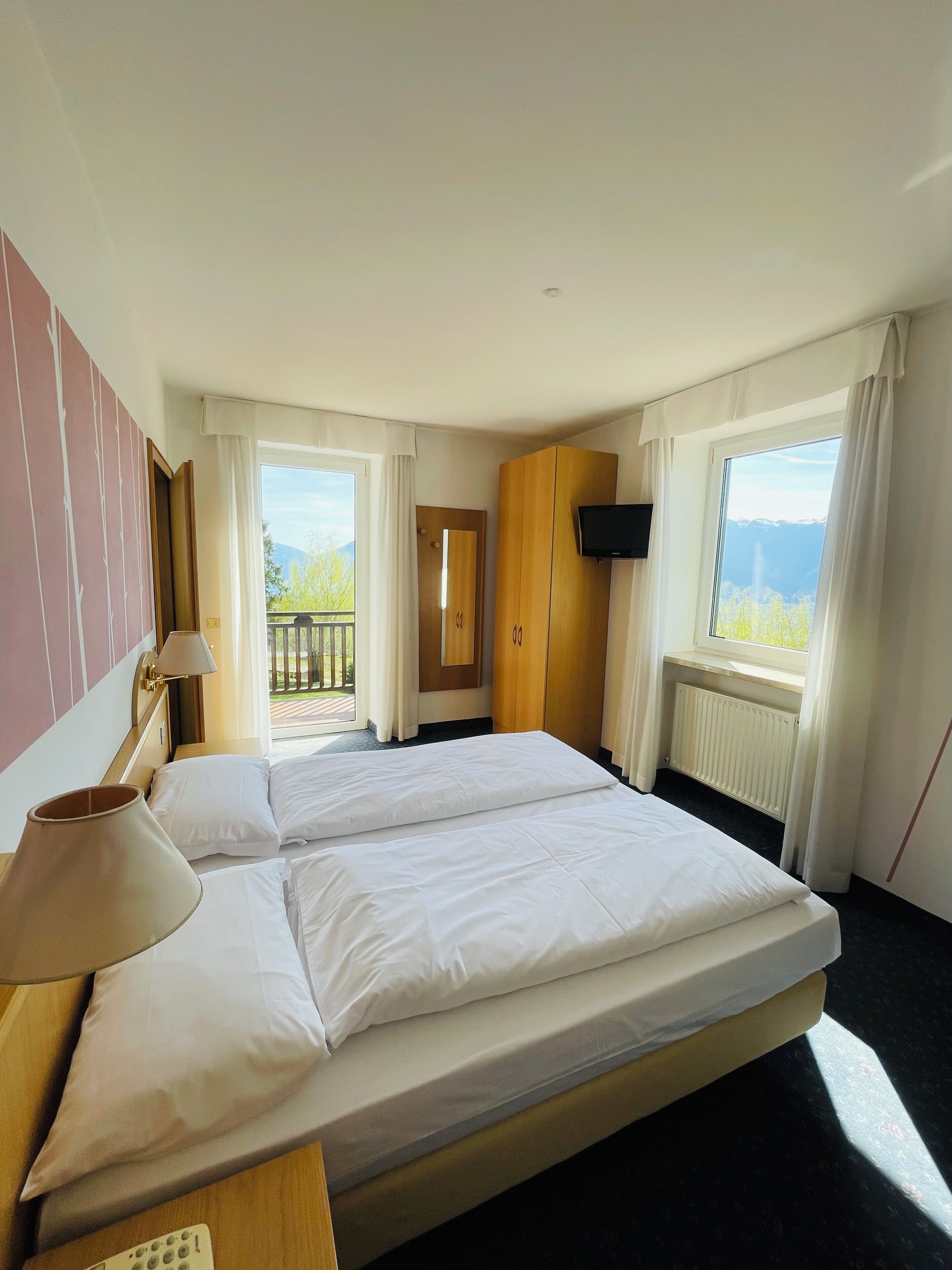 Habitación de hotel con dos camas, televisión, ventana con vistas a las montañas y balcón.
