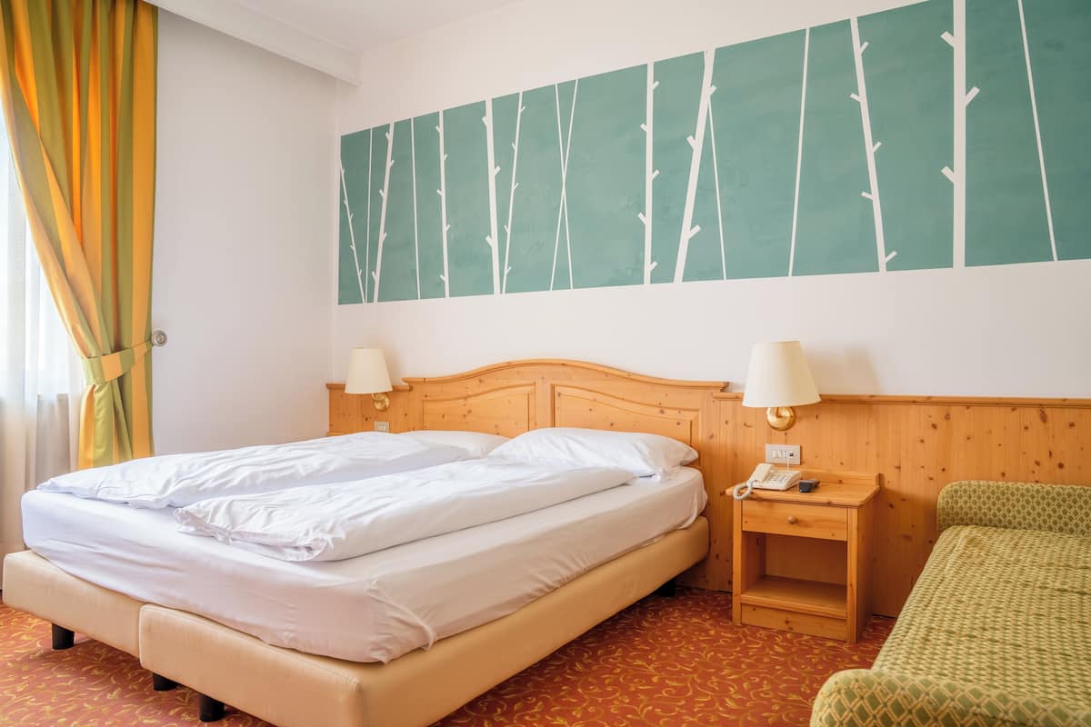 A hotel room with a bed, bedside lamps, a wooden nightstand, and a green chair.