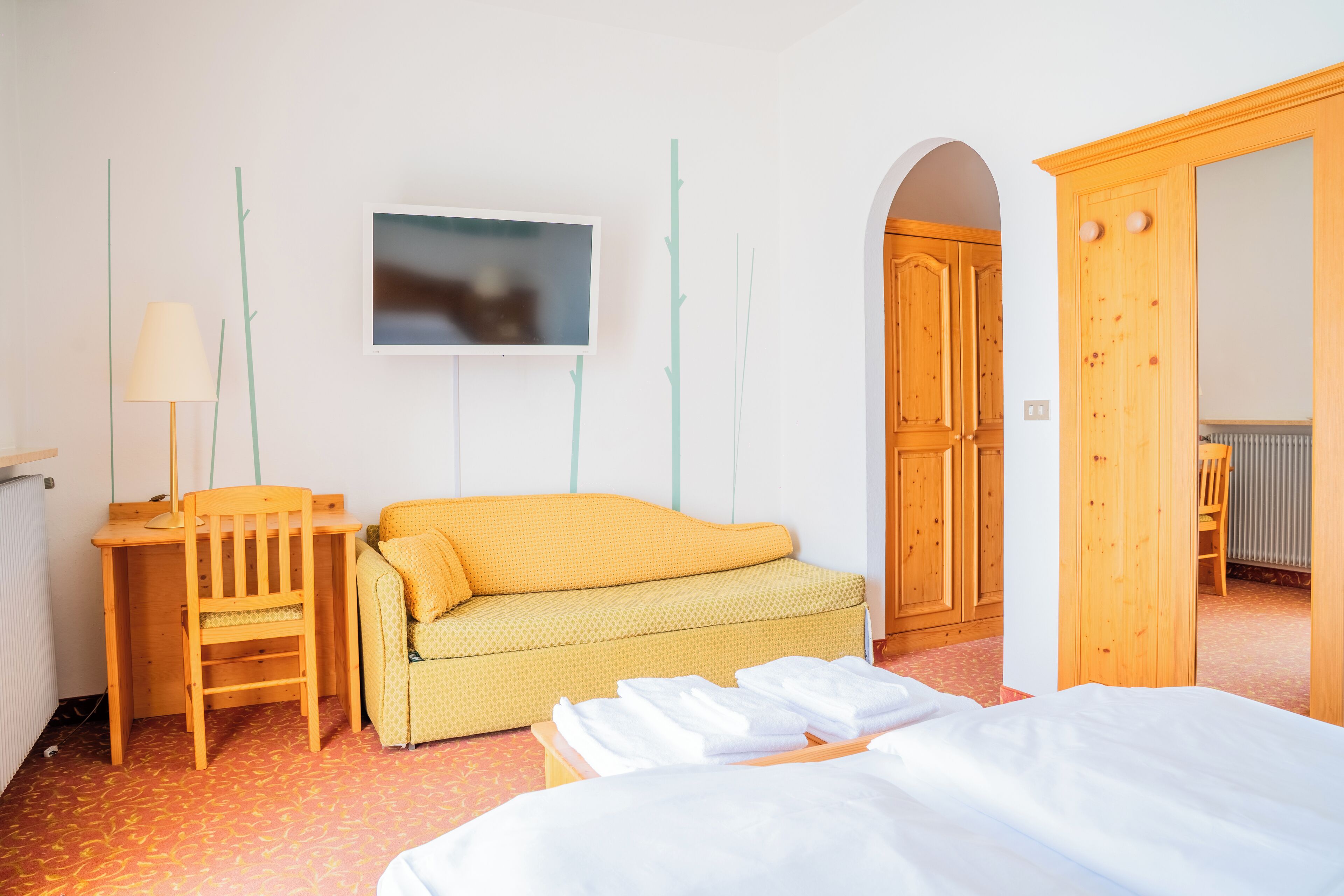 Habitación de hotel con cama, escritorio de madera con silla, sofá y televisor en la pared.