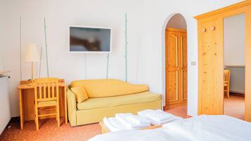Habitación de hotel con cama, escritorio de madera con silla, sofá y televisor en la pared.