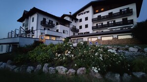 A multi-story building with balconies and a garden area with rocks and flowers. - Enrosadira (Predaia)