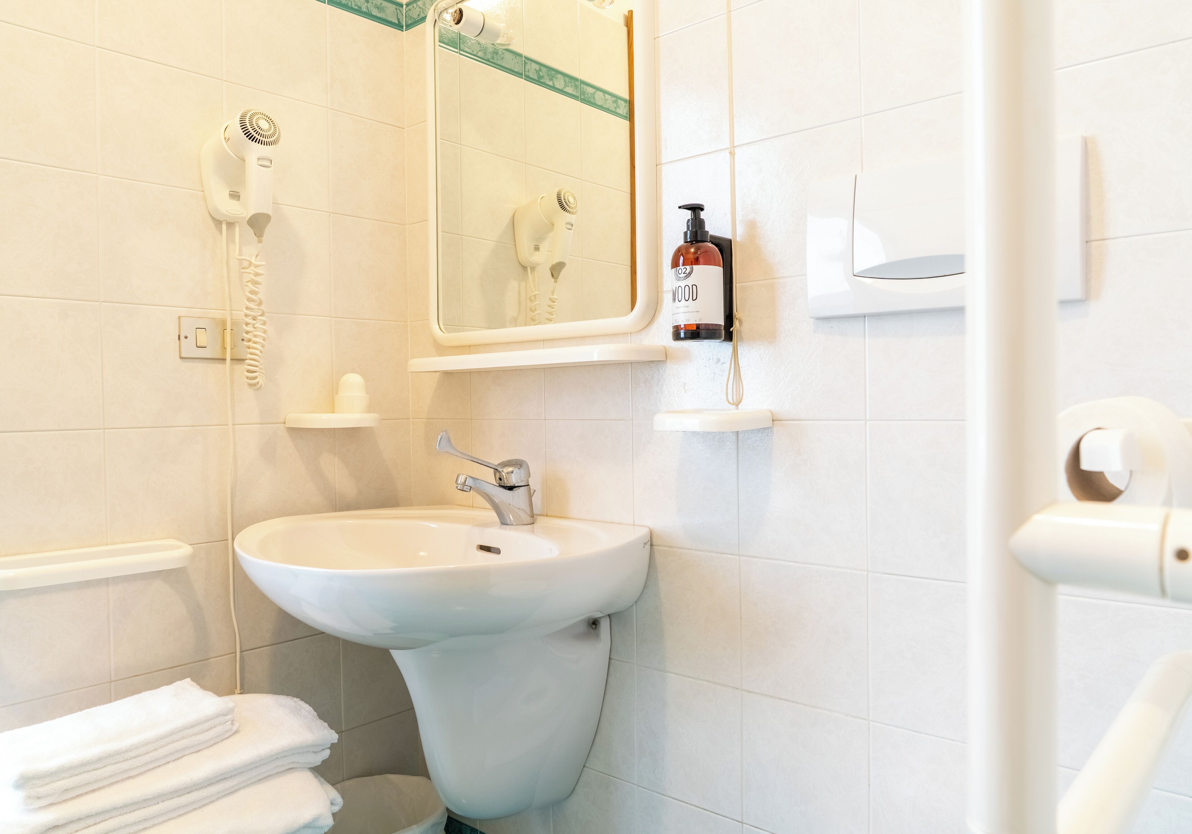 A bathroom with a white sink, a hairdryer mounted on the wall, a mirror, and a bottle of hand soap.