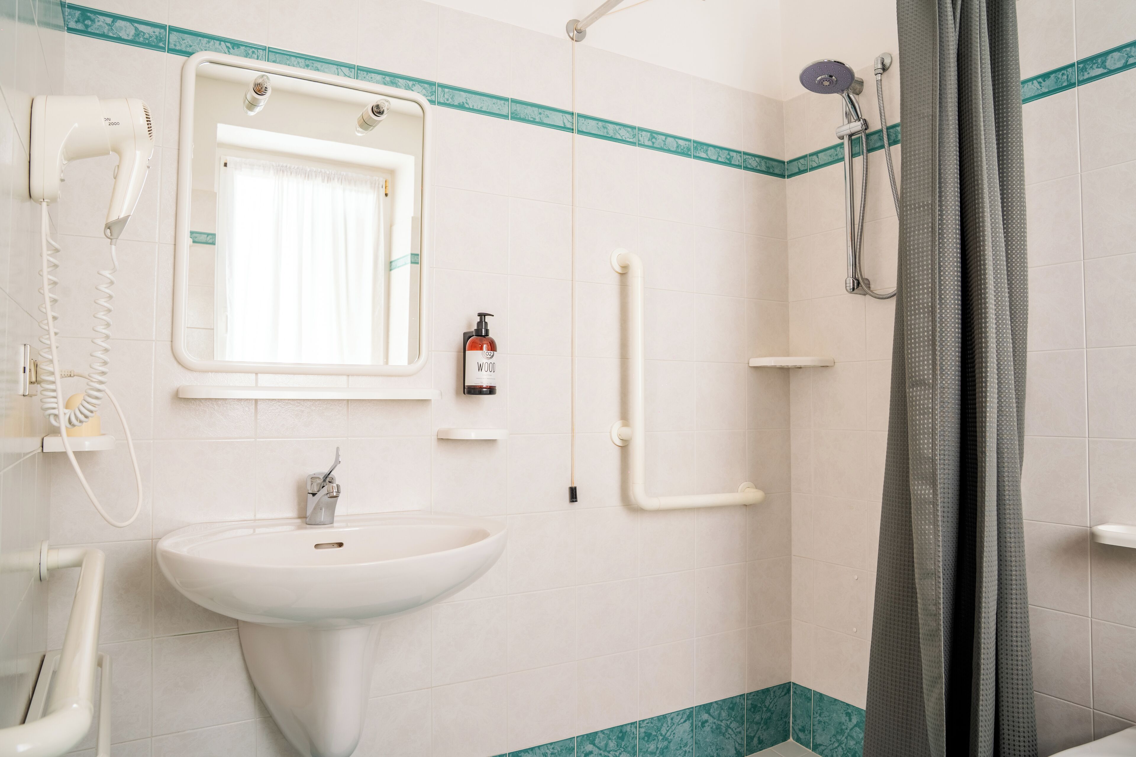 Ein Badezimmer mit Waschbecken, Haartrockner, Dusche und einem Fenster mit Vorhängen.