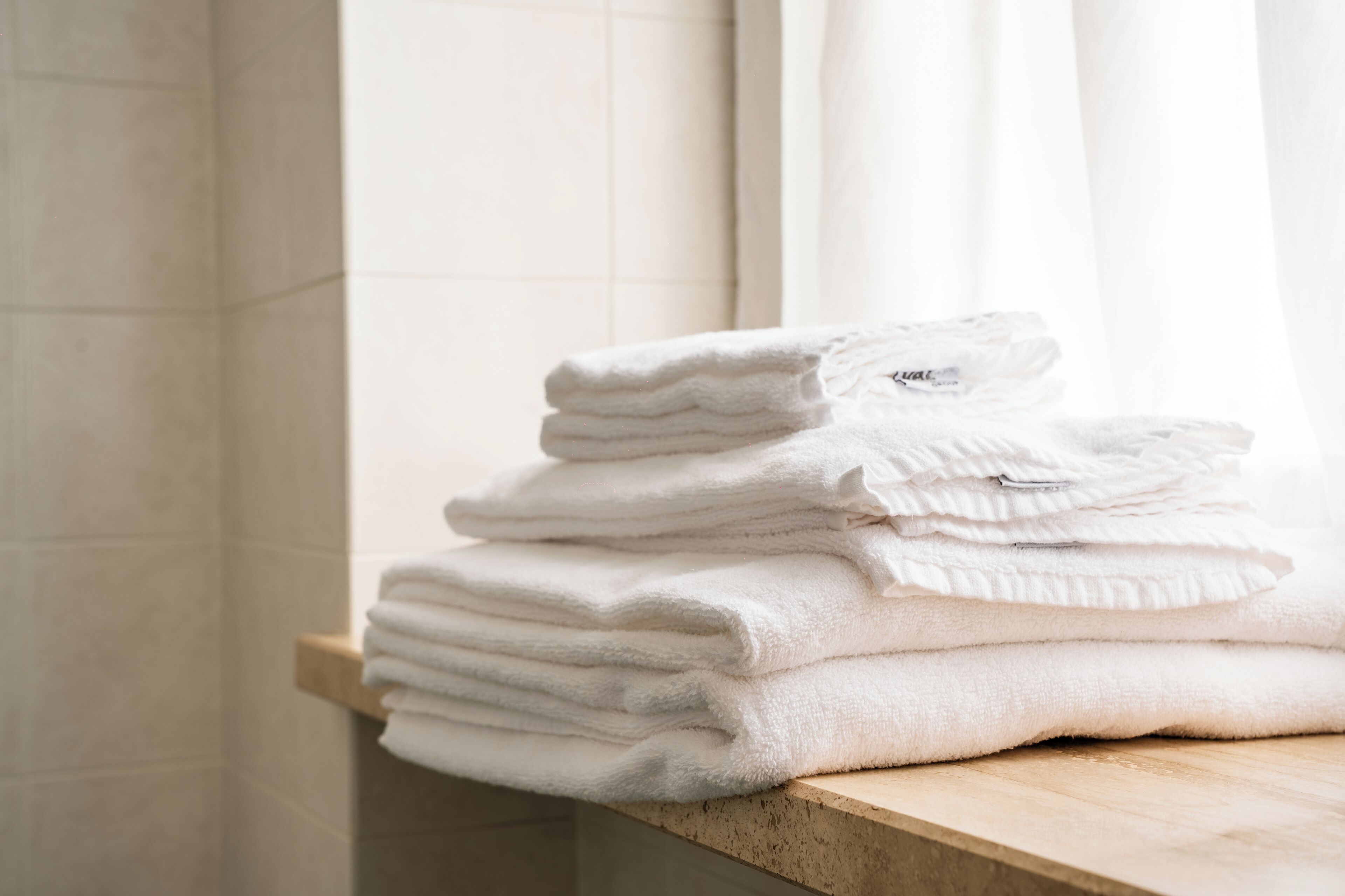 A stack of white towels on a wooden surface in a bathroom with tiled walls.