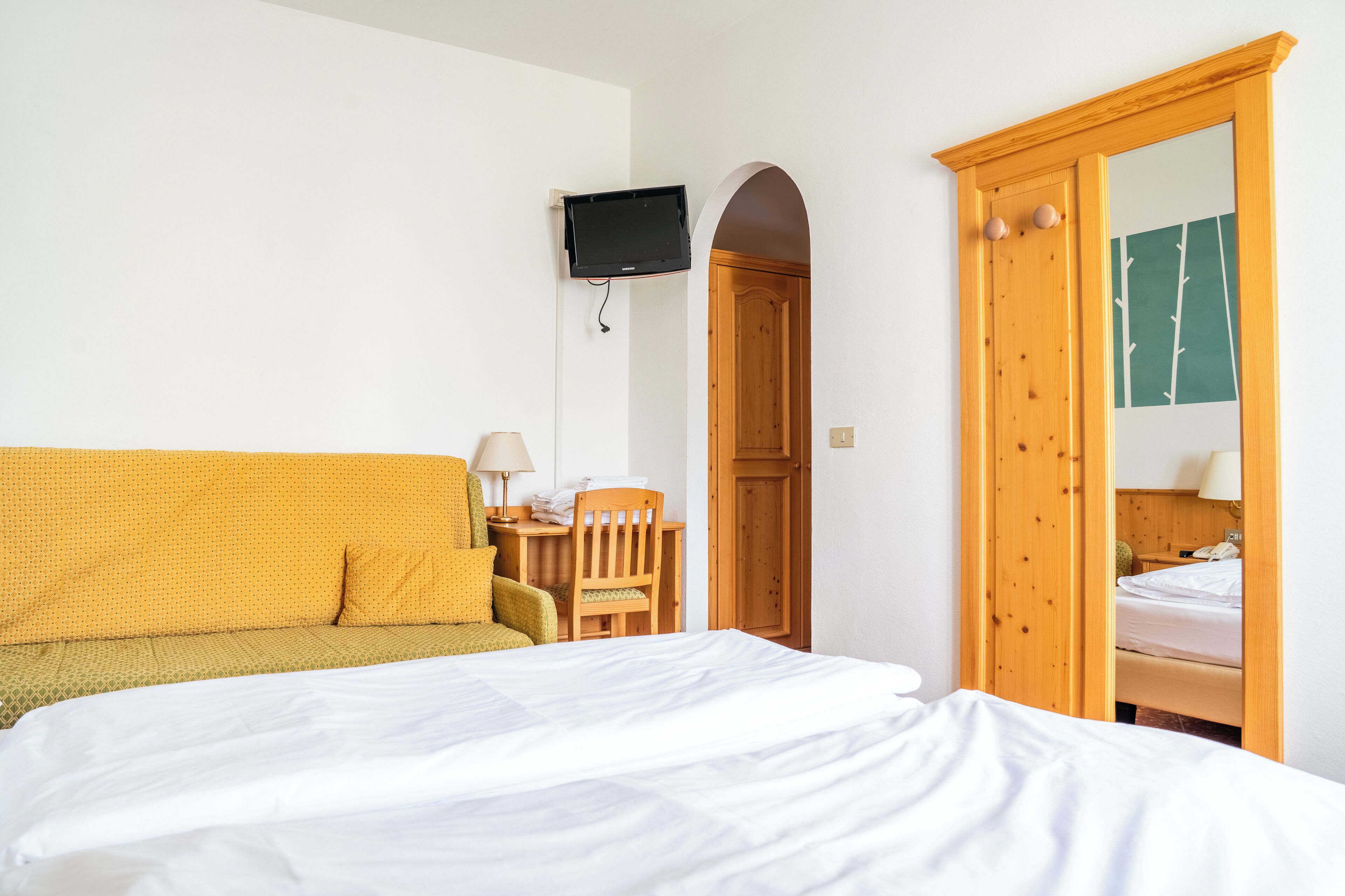 Een hotelkamer met een bed, een bank, een bureau met een lamp en een televisie die aan de muur is bevestigd.