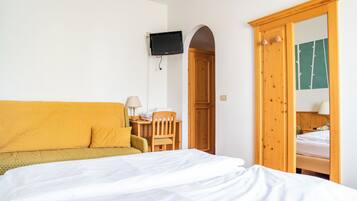 Een hotelkamer met een bed, een bank, een bureau met een lamp en een televisie die aan de muur is bevestigd.