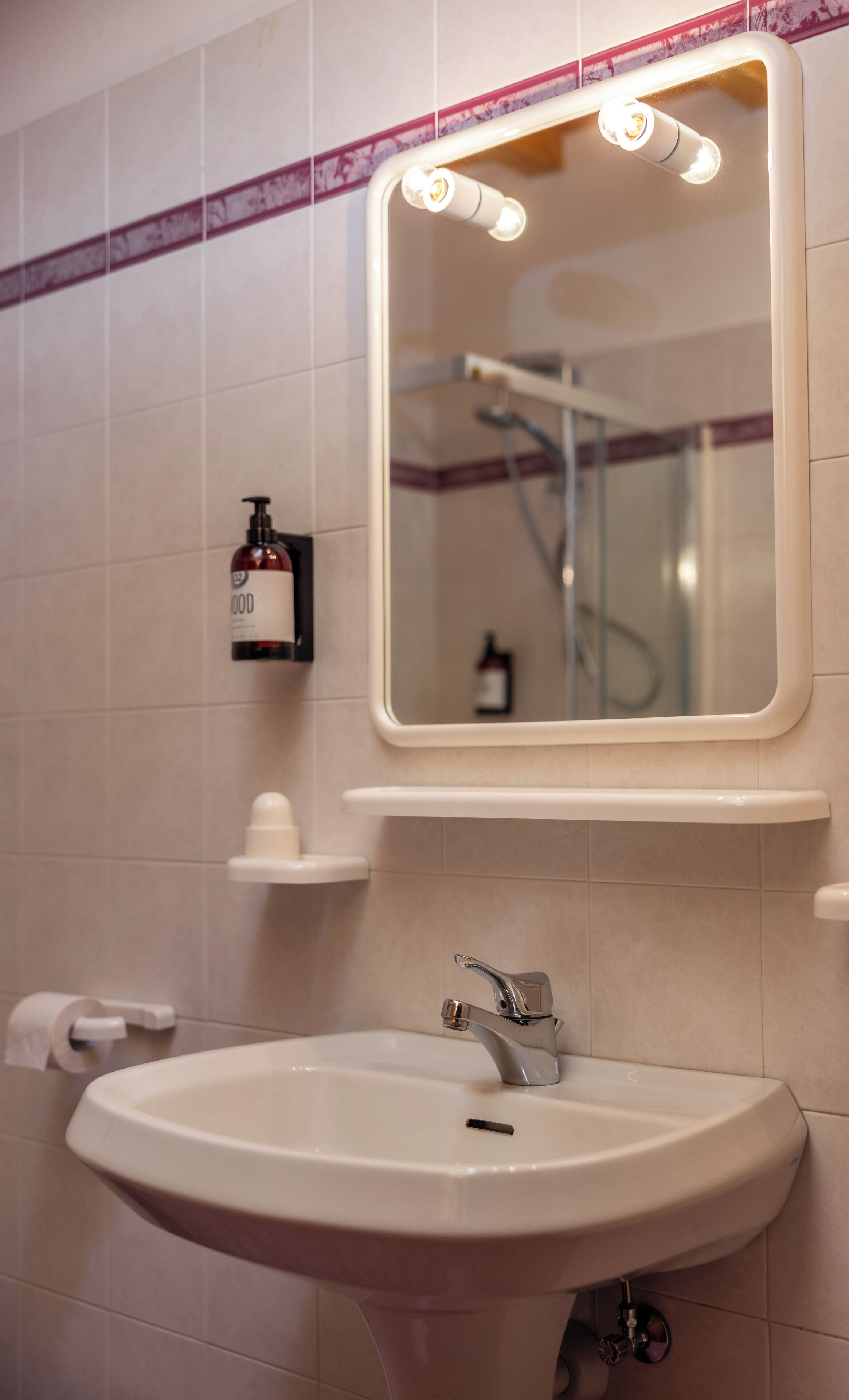A bathroom with a sink, mirror, and a soap dispenser on the wall.