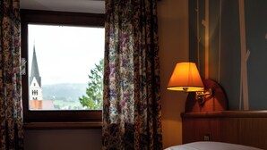 A hotel room with a bed, a window with floral curtains, and a lamp on a bedside table. - Enrosadira (Predaia)