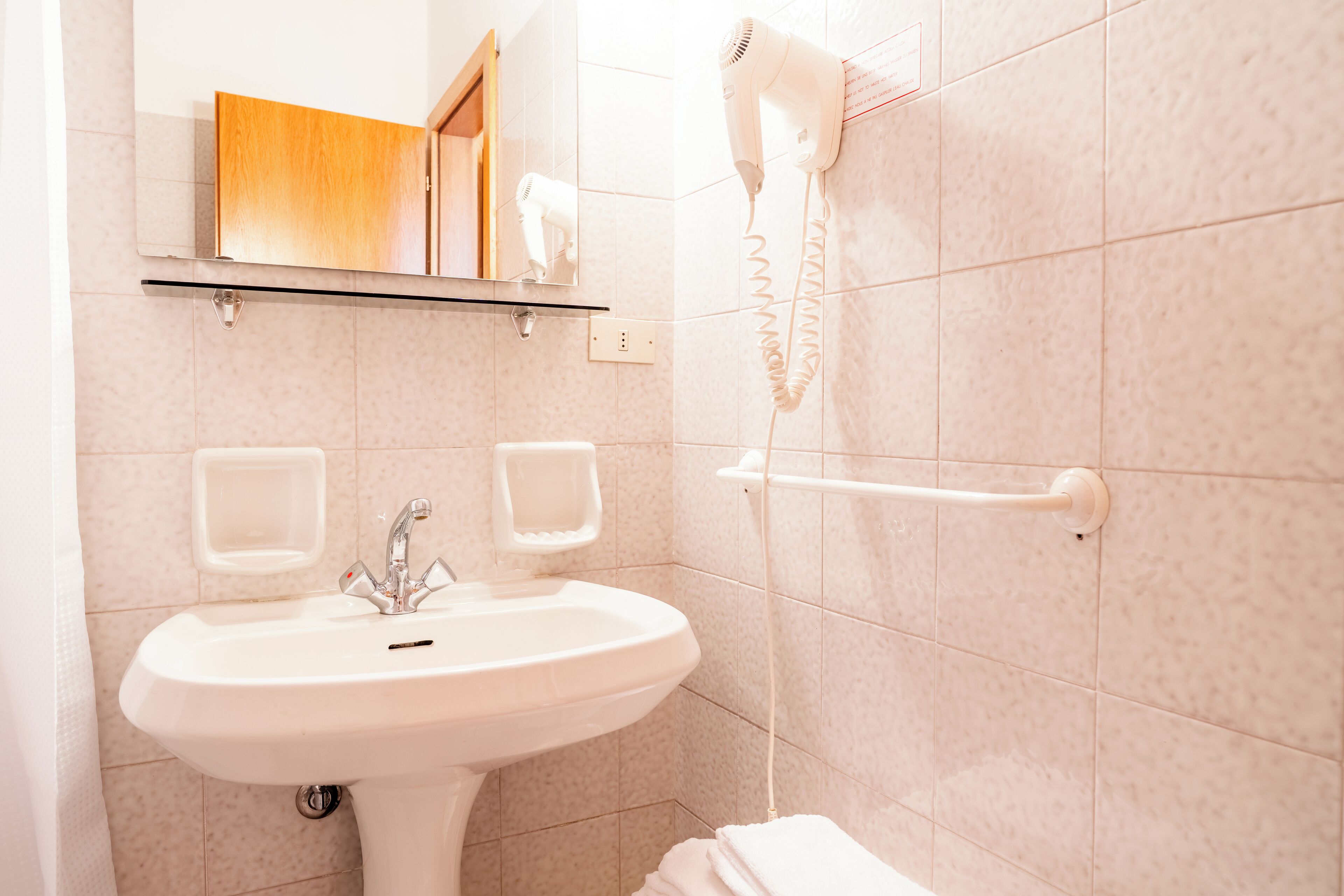 Une salle de bain avec un lavabo blanc, un miroir, un sèche-cheveux fixé au mur et un porte-serviettes.