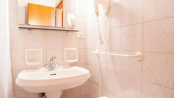 Une salle de bain avec un lavabo blanc, un miroir, un sèche-cheveux fixé au mur et un porte-serviettes.